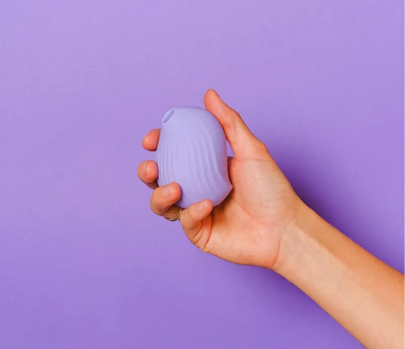 A hand holding a violet suction vibrator in front of a violet background