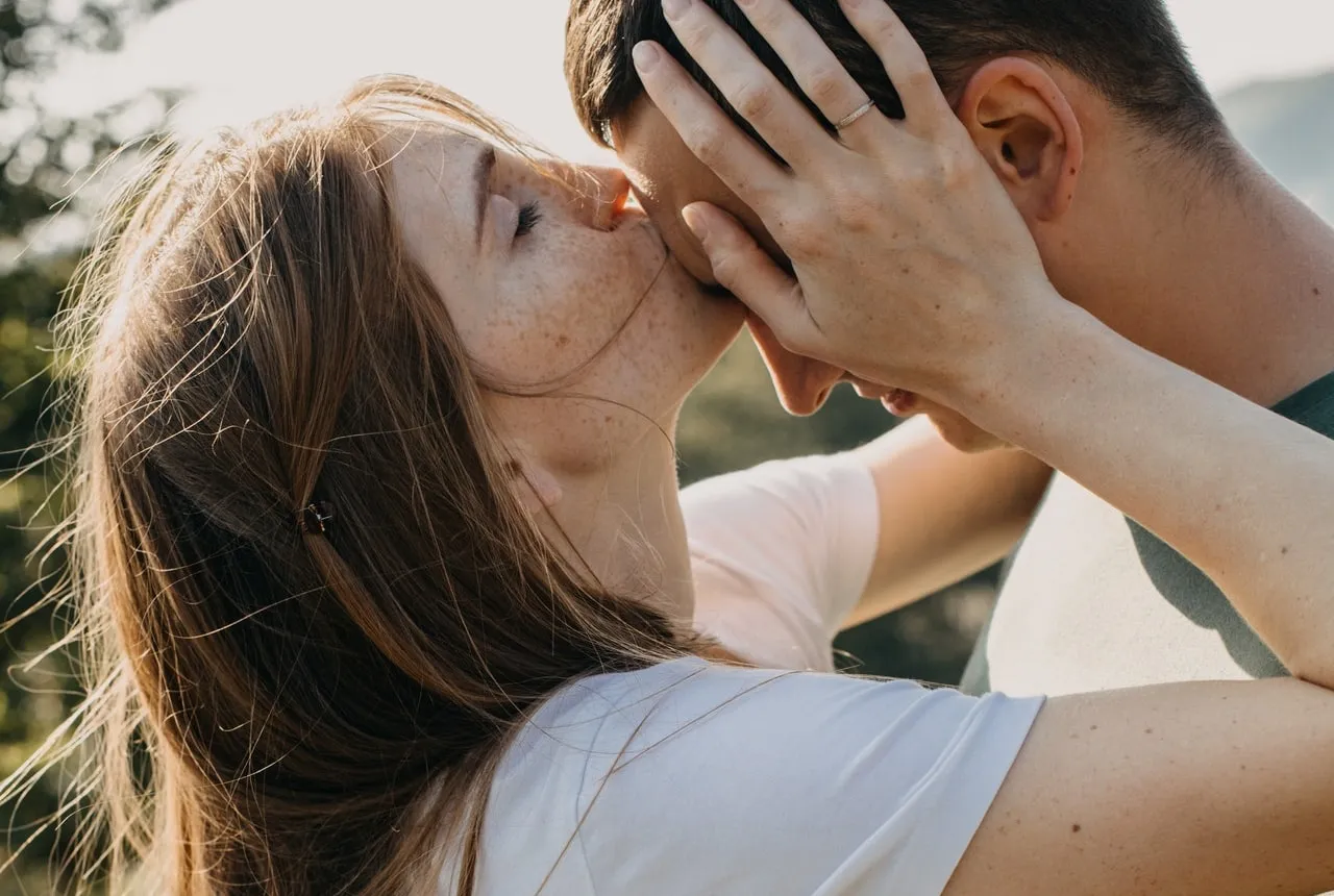 A young woman kissing a young man on his forehead