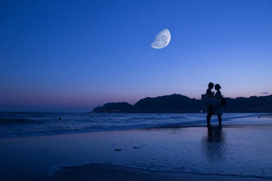 Two humans romantically facing each other at the beach with the moon shining